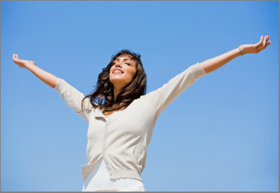 Pretty young woman with arms raised against blue sky